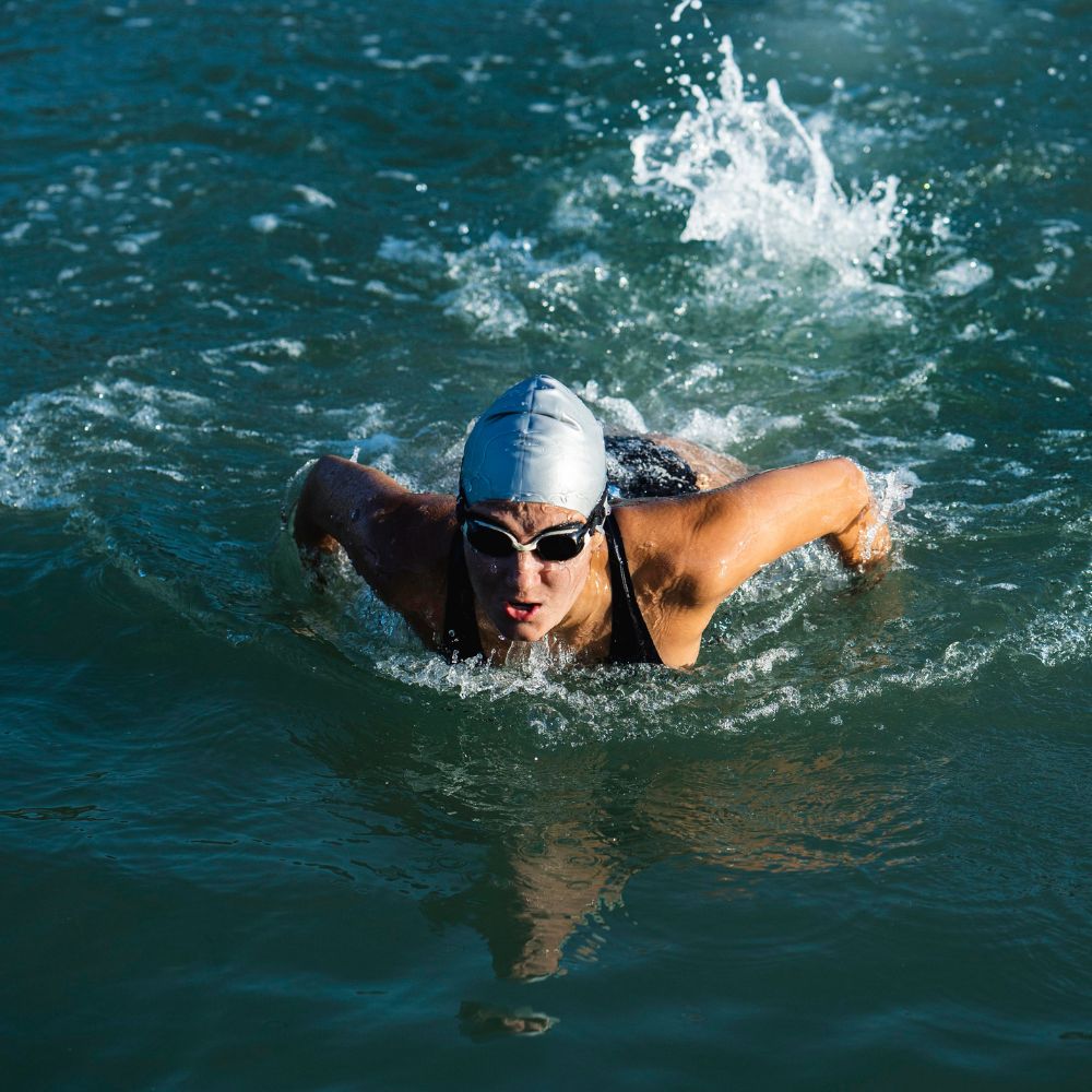 Person swimming in open water wearing a swim cap and goggles.