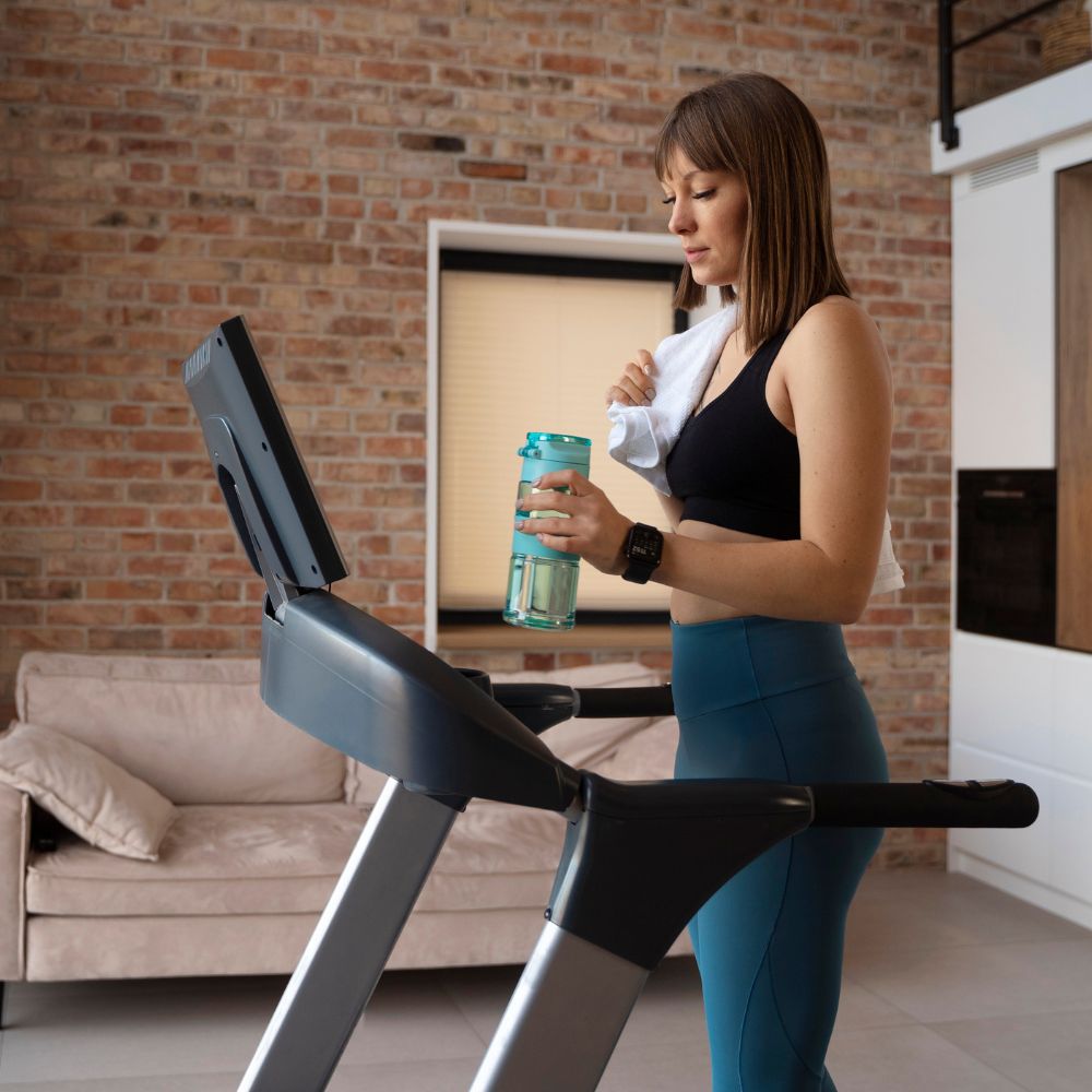 Woman on a treadmill in a home setting holding a water bottle.
