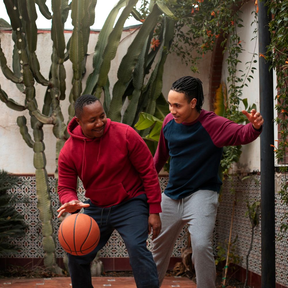 Two men playing basketball outdoors with cacti and plants in the background