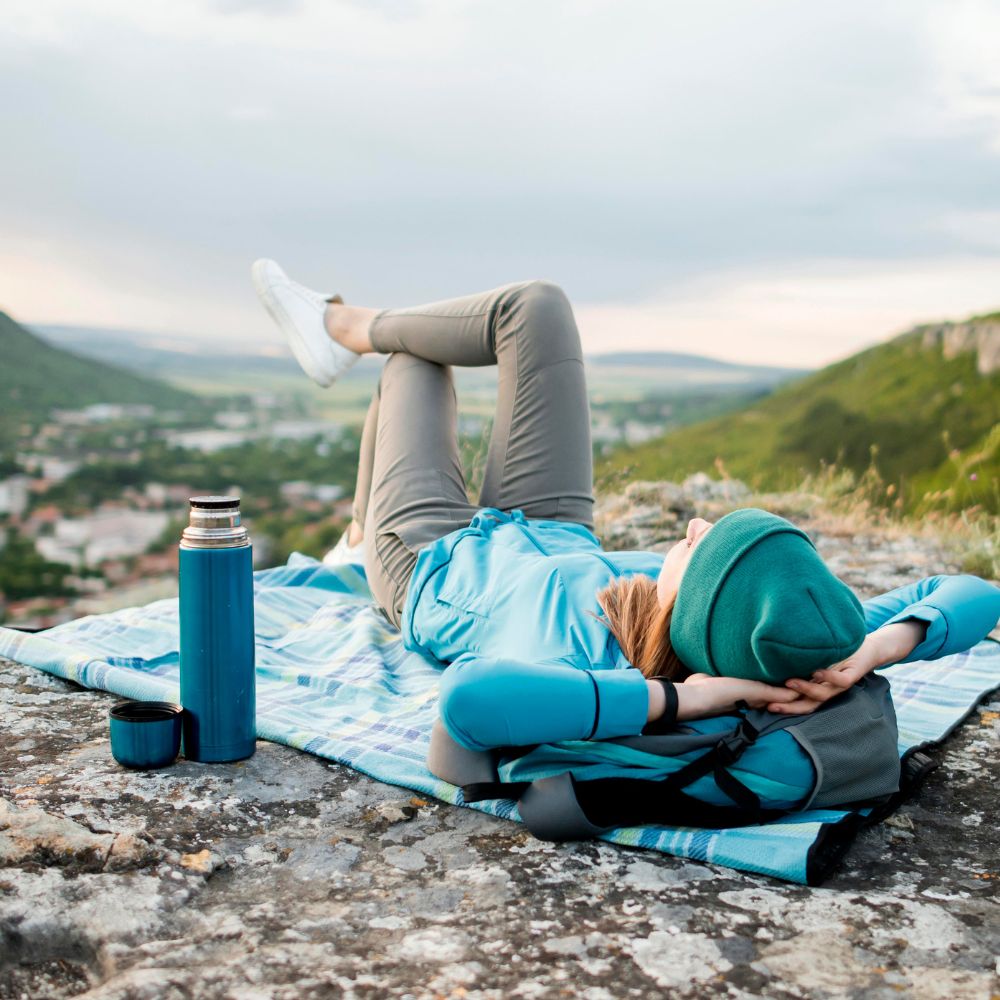 Person lying on a blanket with a scenic view, wearing a blue jacket and gray pants.